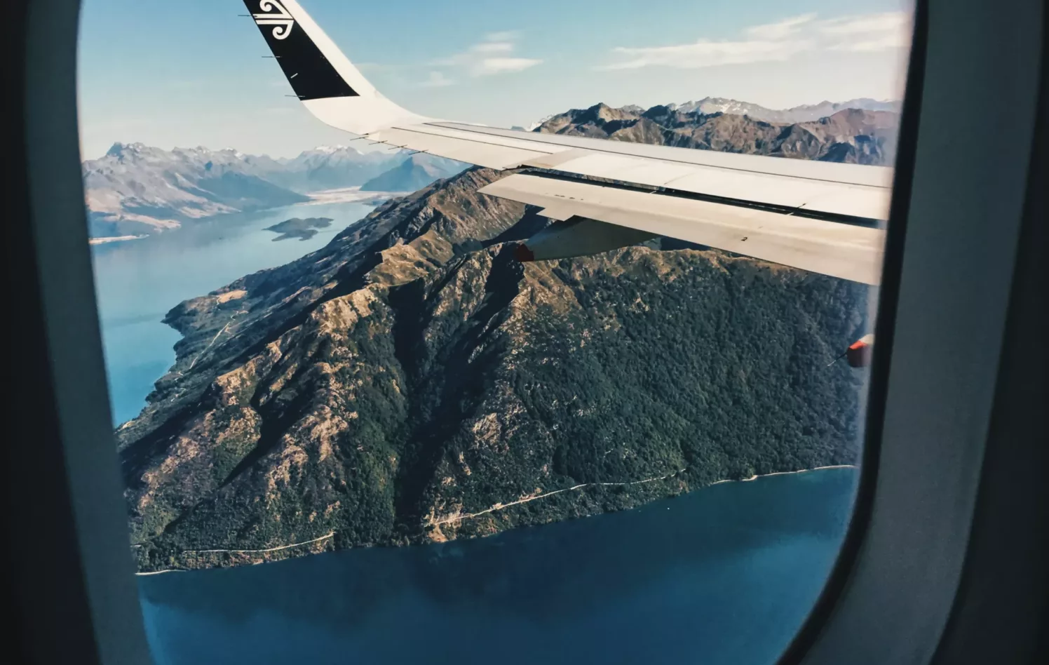 Utsikt fra flyvindu av flyvinge, sjø og fjell
