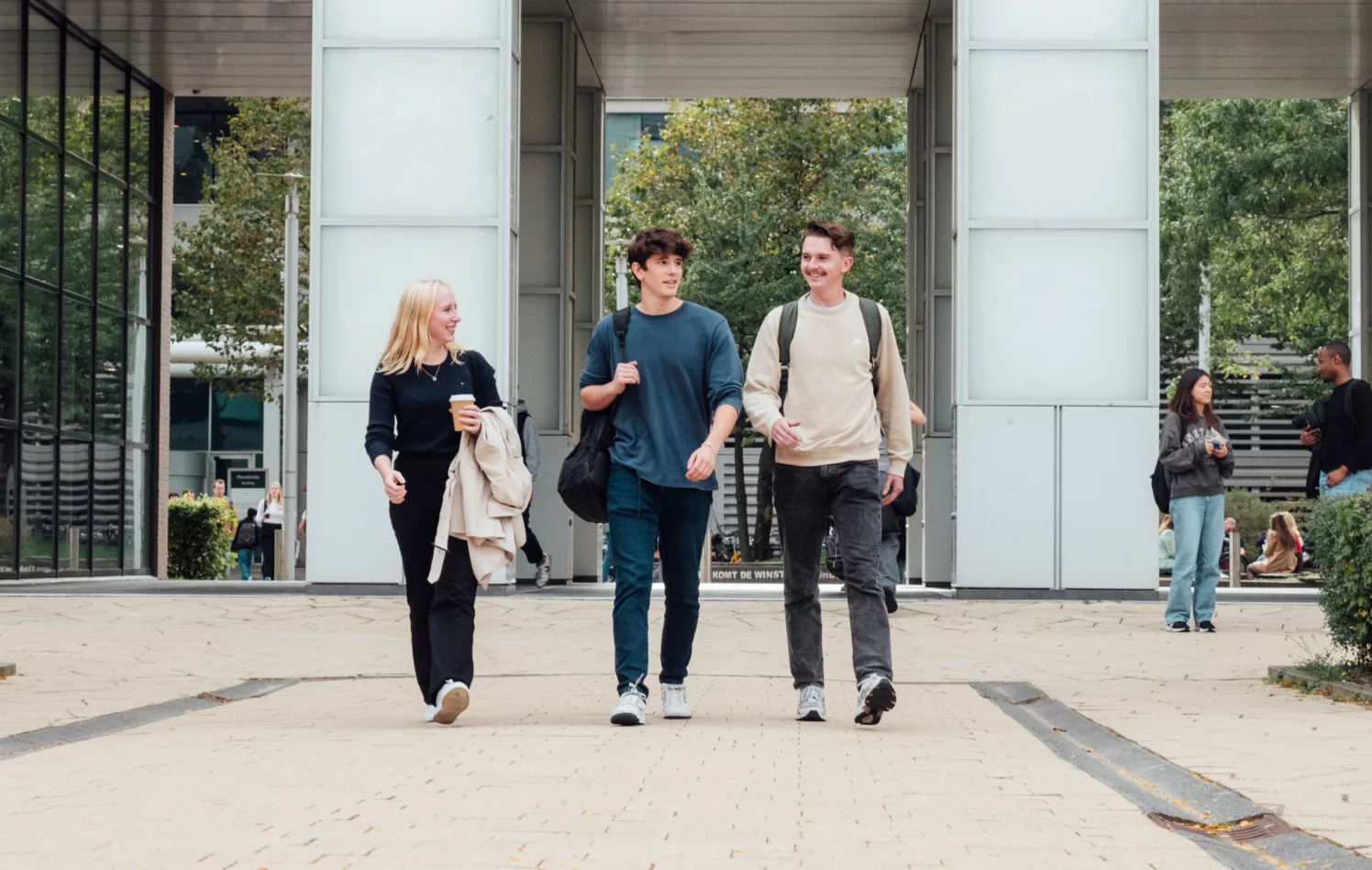 Tre studenter går nedover vei foran skolebygg